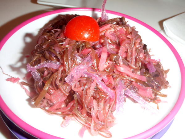 Merileväsalaatti japanilaisessa kaiten-sushiravintolassa, jossa annokset kulkevat hihnalla edessä. Siitä voi poimia annoksia tai tilata niitä menusta erikseen. Hinnat määräytyvät lautasen värin mukaan. Tämä merileväsalaatti oli samanmakuista kuin wakamesalaatit yleensäkin, mutta vihreän sijaan punasävyistä. Lue lisää merilevän syömisestä maailmalla >>