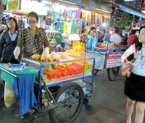 Näitä hedelmäkärryjä on Bangkokissa kaikkialla. Hedelmäpussin hinta turisteille vaikuttaa olevan vakio 20 bahtia, mutta puolikkaan ananaksen olen saanut 15 bahtillakin ja jossain paikoissa turistilta yritetään pyytää 30-40 bahtiakin. Muiden hedelmäkärryjen myyjät eivät ole näin hipstereitä kuin tämä KSR:n myyjä. 