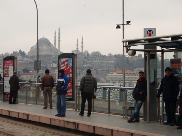 Ukkoja Galata Köprüsün sillalla Karaköyn ratikkapysäkillä. Takana Sultanahmetin kaupungiosaa ja pari moskeijaa, mm. Suleimanin moskeija.